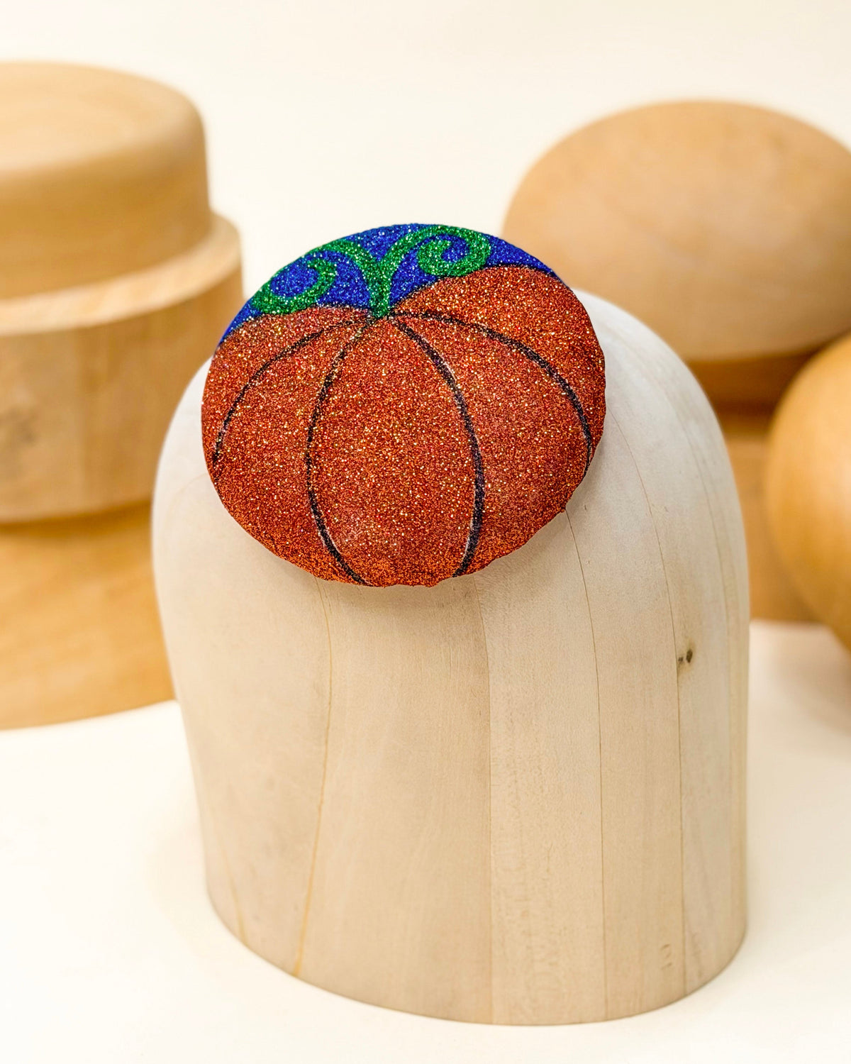 A glitter fascinator hat made to resemble a pumpkin by Desiree Spice. Autumn and halloween inspired pillbox hat sitting on top of a wooden millinery hat block.